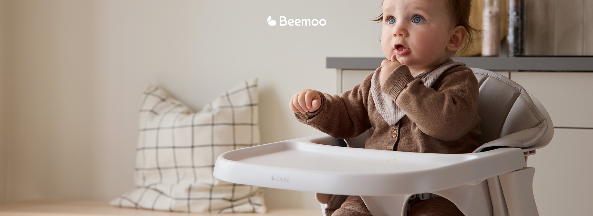 Barn sitter i høy stol med teksten 'Beemoo'.