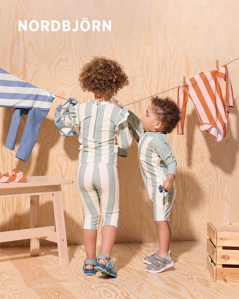 Barn med solhatt leker med bøtter på en treterrasse.