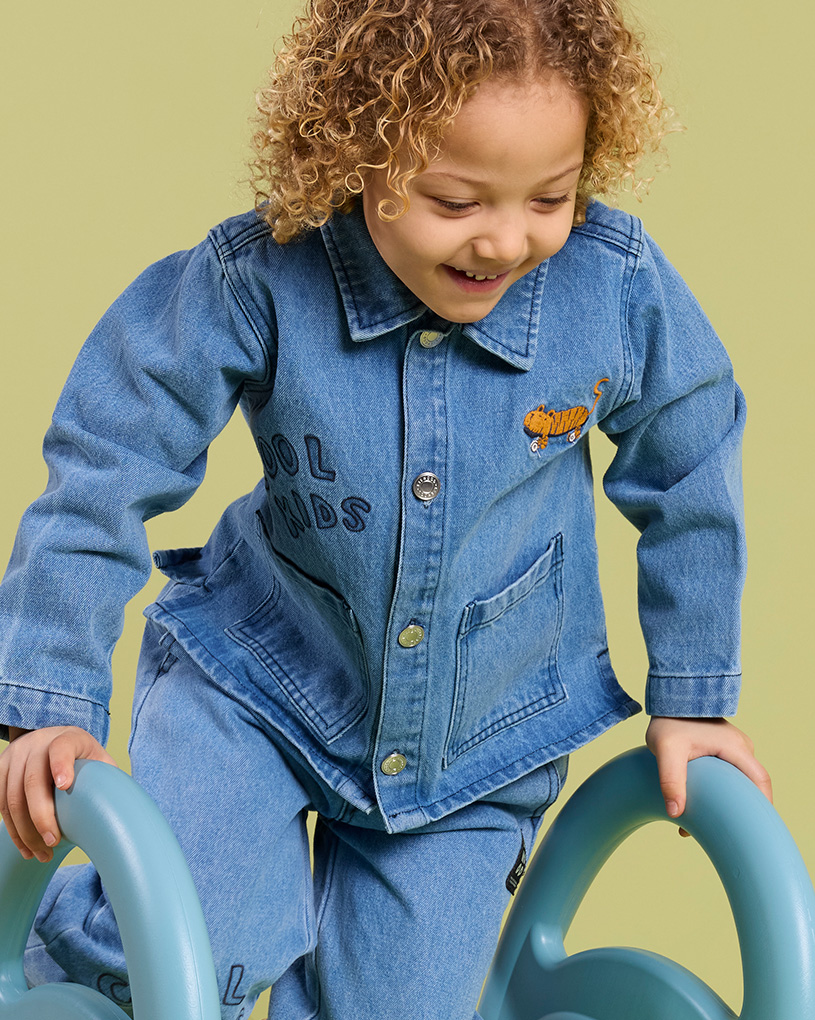 Barn i denimjakke med teksten 'COOL KIDS', som leker på en blå leke.